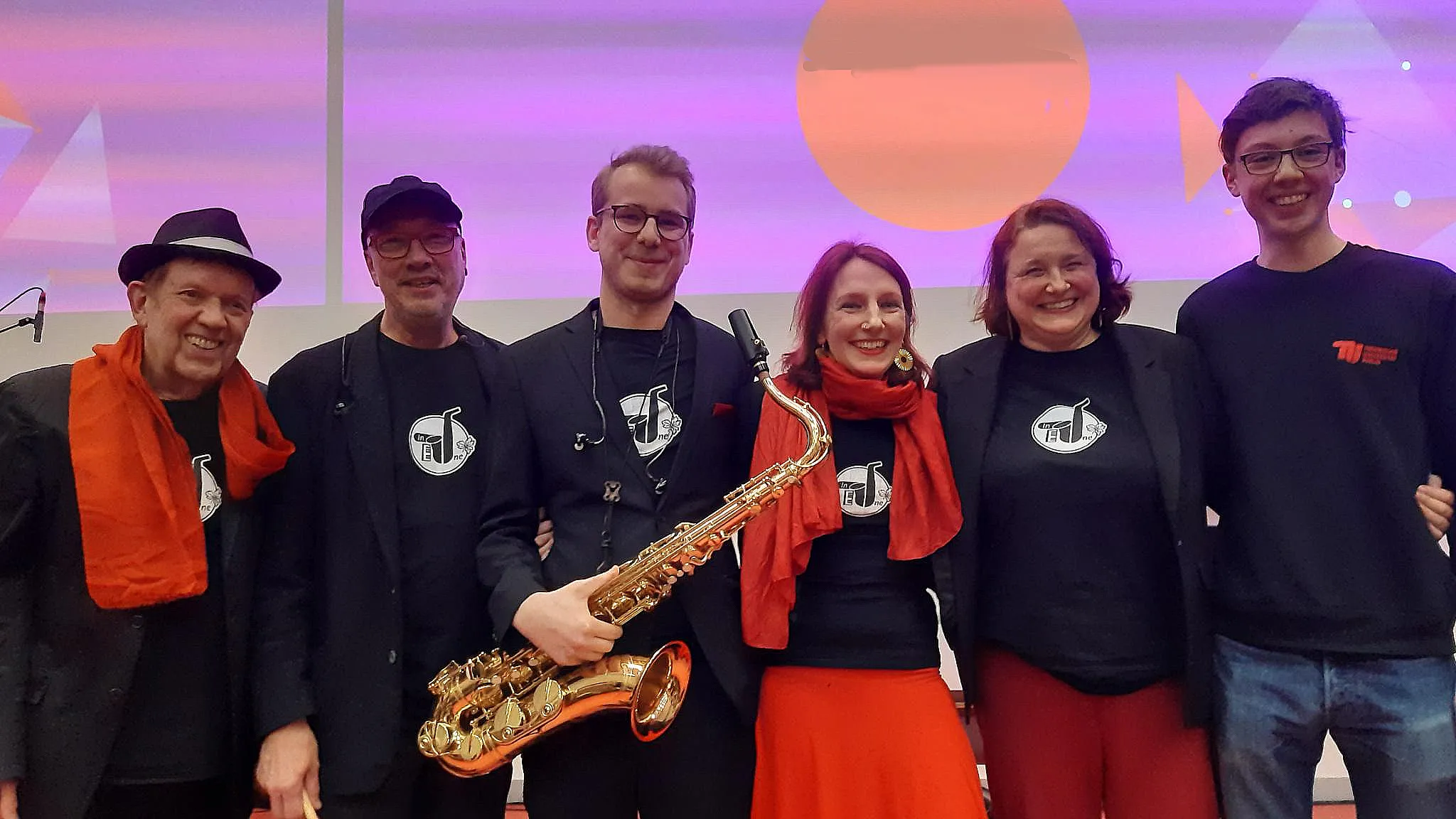 Sechs Mitwirkende nach der Preview, eine Person mit Saxophon, mehrere mit roten Schals